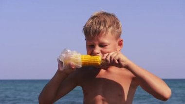 Çocuk deniz kıyısında mısır yiyor..