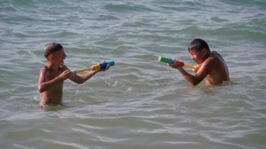 Çocuklar denizde su tabancalarıyla oynarlar..