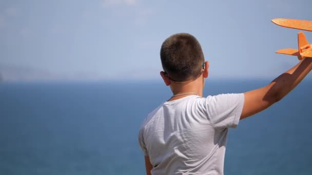 Pojke med en leksak flygplan i händerna på bakgrunden av havet. — Stockvideo