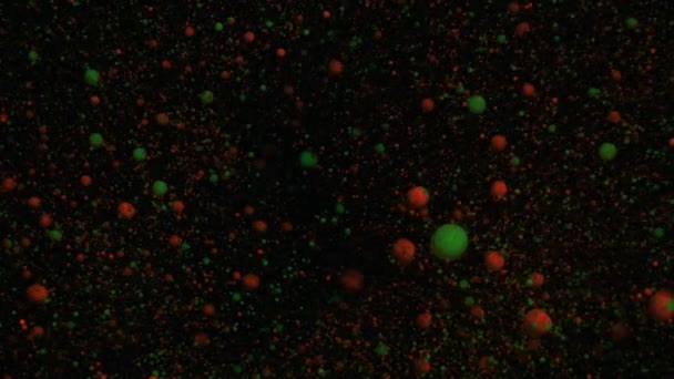 Pomerančové a zelené objemové fluorescenční částice se pohybují a mění na černém pohyblivém pozadí, přechod. — Stock video