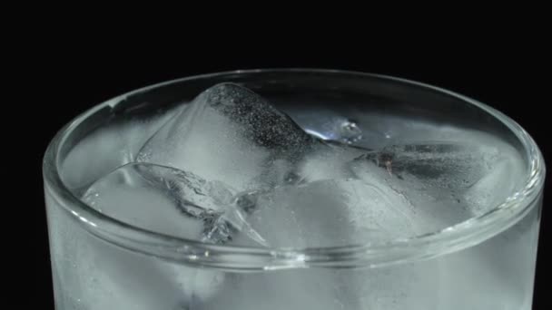 Lasi on täynnä soodavettä. Kuplia kivennäisvedessä. Jääkuutiot lasissa mustalla pohjalla. — kuvapankkivideo