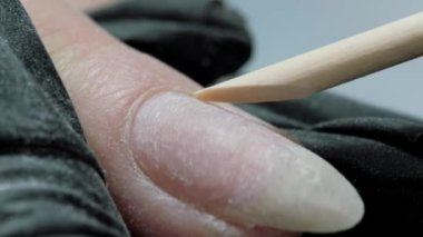 Tırnak derisini tahta turuncu bir sopayla kaldırıyor. Donanım birleşik manikür. Manikür bakım prosedürü.