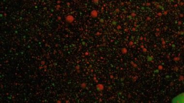 Turuncu ve yeşil hacimli floresan parçacıkları siyah hareket eden bir zemin üzerinde hareket eder ve değişir, geçiş.