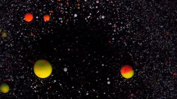 Boules rondes multicolores sur fond noir avec paillettes argentées. Les particules blanches, jaunes et rouges se déplacent au hasard. — Video