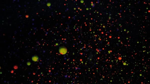 Runda flerfärgade bollar på en svart bakgrund med silver paljetter. Röda, blå och gröna partiklar rör sig slumpmässigt. — Stockvideo