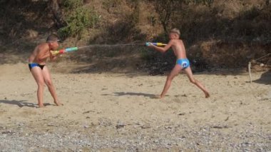 Çocuklar deniz sahilinde su tabancalarıyla oynuyorlar..