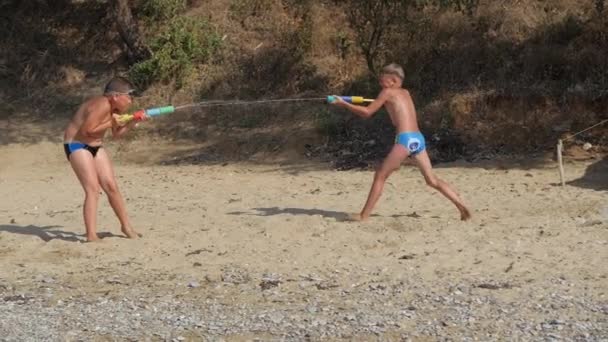 Jongens spelen met waterpistolen op het strand. — Stockvideo