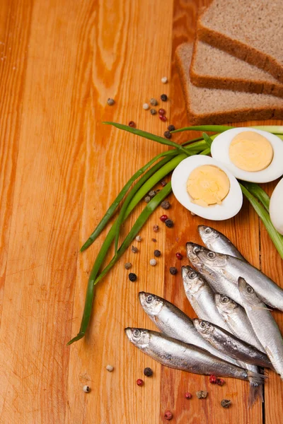 Anchovas salgadas, ovo, pão e cebolinha na madeira — Fotografia de Stock