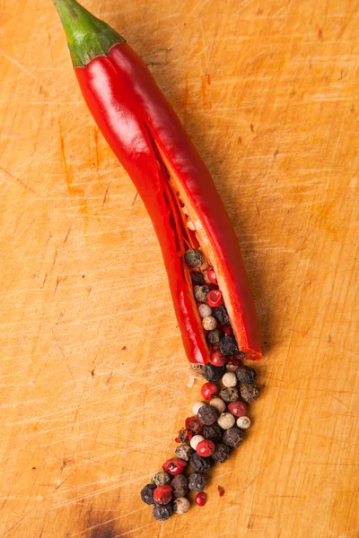 Cut capsicum chili pepper and peppercorn on wooden board — Stock Photo, Image