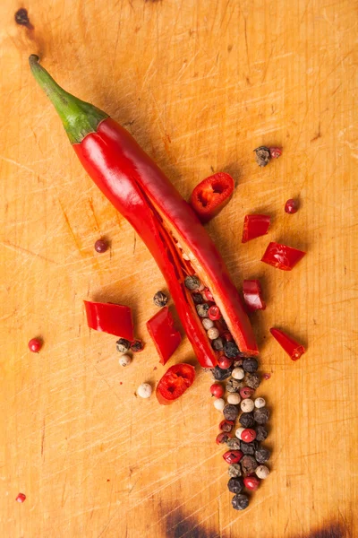 Cut capsicum chili pepper and peppercorn on wooden board — Stock Photo, Image