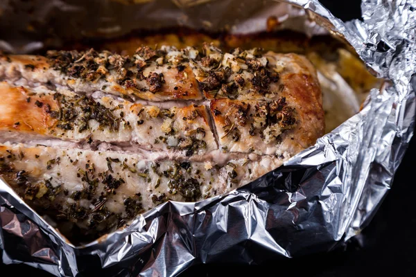 baked meat with seasoning in foil on black tray