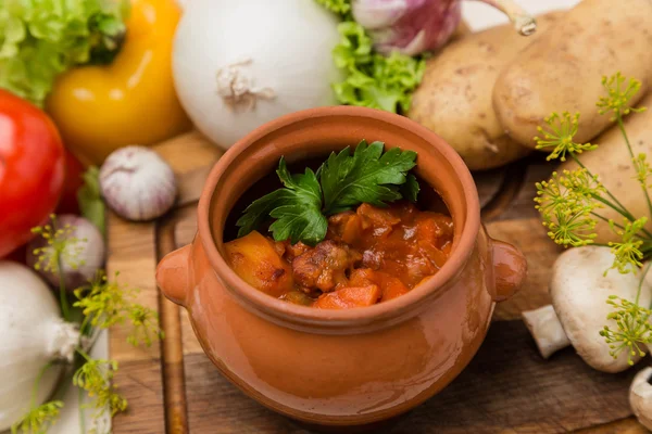 Hot roast in pot with garnish on wood board — Stock Photo, Image