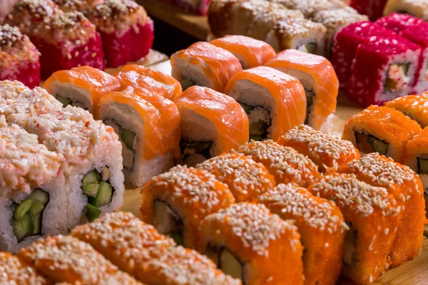 Sushis assortis et rouleaux sur panneau de bois dans la lumière sombre — Photo