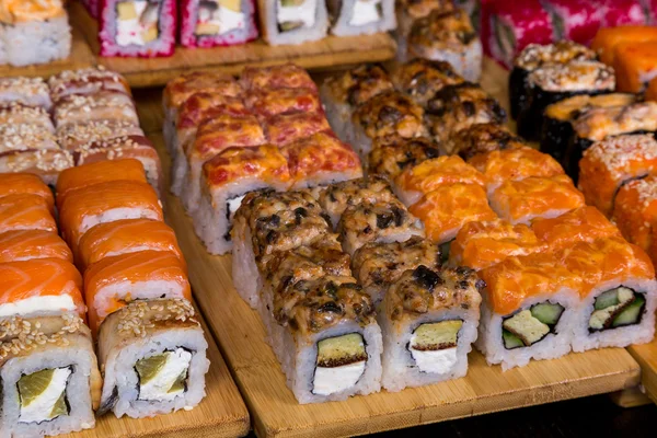 Surtido de sushi y rollos en tablero de madera en la luz oscura — Foto de Stock