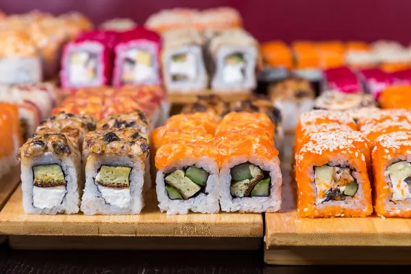 Sushis assortis et rouleaux sur panneau de bois dans la lumière sombre — Photo