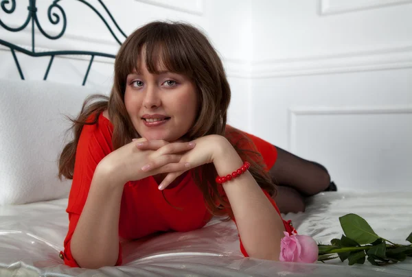 Vacker flicka i röd klänning på sängen — Stockfoto