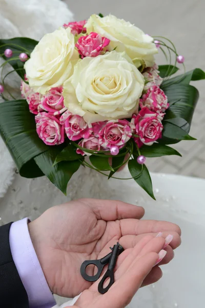 Γαμπρός χέρια που κρατούν τα κλειδιά και χέρι τη νύφη με μια ανθοδέσμη της νύφης — Φωτογραφία Αρχείου