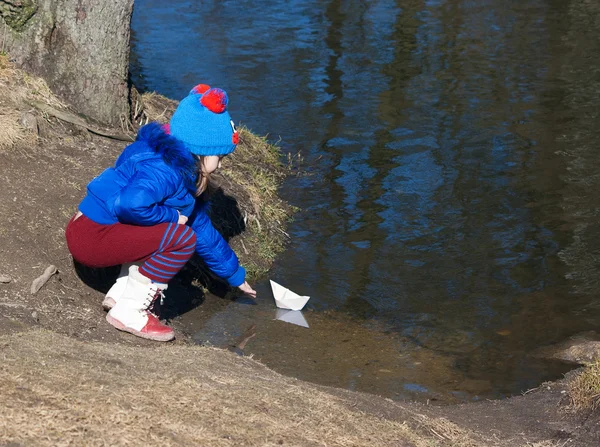 Liten flicka spelar med papper båt på floden — Stockfoto