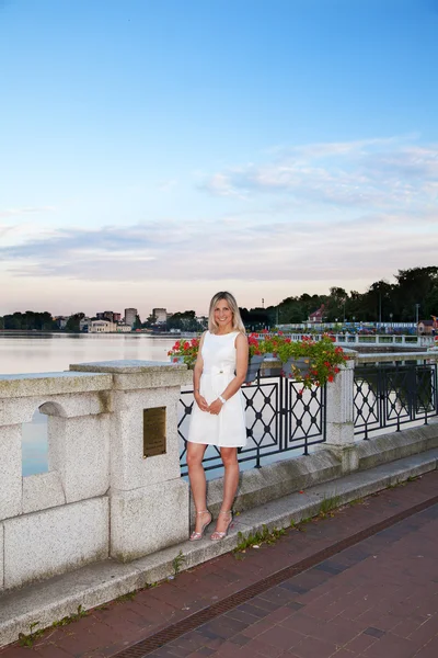 Jovem mulher em um vestido branco perto do lago ao pôr do sol — Fotografia de Stock