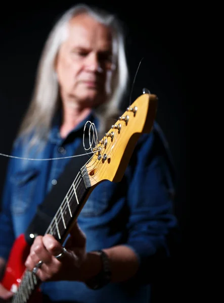 青のデニムシャツを着た長髪の白髪の老人が黒を背景にエレキギターを弾く — ストック写真