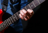 starší muž v modré džínové košili hraje na elektrickou kytaru na černém pozadí. detailní záběr