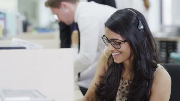 Vrolijke jonge klant dienst exploitant op het werk in een drukke callcenter — Stockvideo