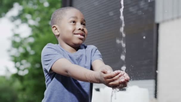 Счастливый, улыбающийся африканский мальчик наслаждается ощущением пресной воды на руках — стоковое видео