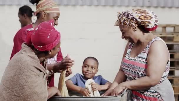 Familia africana y miembros de la comunidad trabajan juntos, lavando la ropa a mano — Vídeo de stock