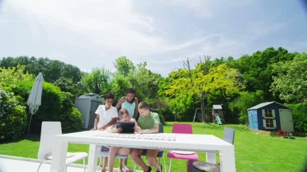 Jóvenes amigos en el jardín en un día de verano jugando con una tableta de ordenador — Vídeos de Stock