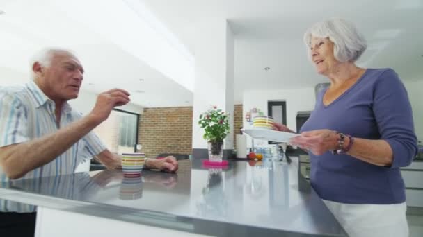 Feliz casal aposentado desfrutar de bebidas quentes e biscoitos em sua cozinha moderna — Vídeo de Stock