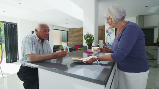 Boldog nyugdíjas pár élvezze a forró italok és kekszek a modern konyha — Stock videók