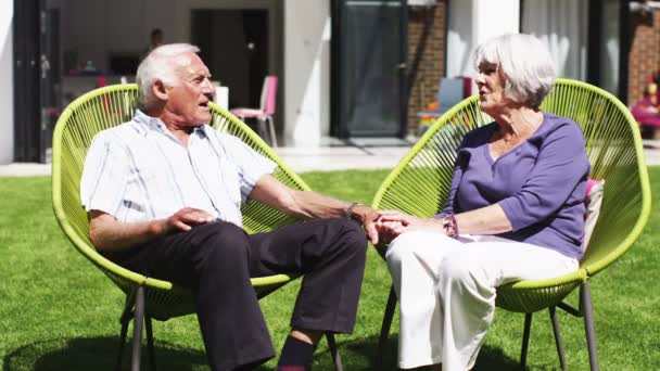 Nyugdíjas házaspár ül, és kéz a kézben pihenhetnek a kertben — Stock videók