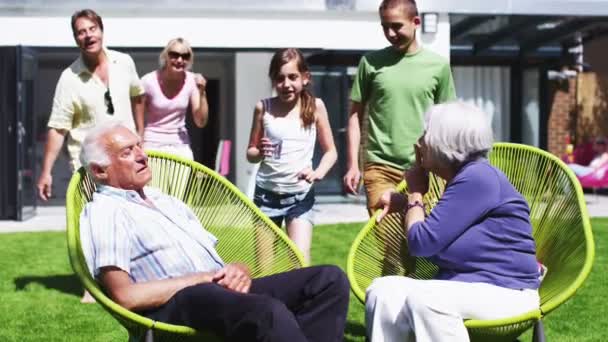 Grandfather plays a trick on his family as they sit in the garden at home — Stock Video