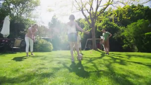 Молодая девушка играет в футбол со своей семьей на открытом воздухе в солнечный день — стоковое видео