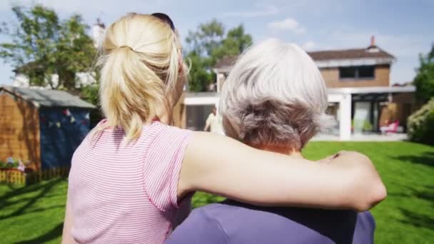 Hija y su anciana madre se unen mientras ven a la familia jugar en el jardín — Vídeo de stock