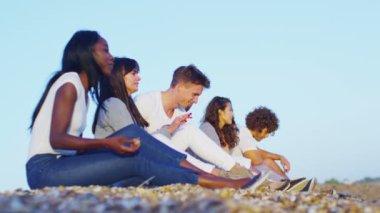 kumsalda oturuyor ve taş atan arkadaşlar