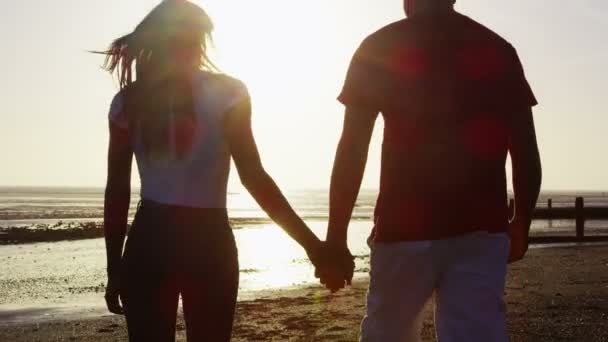 pár drží za ruce a chůze na pláž