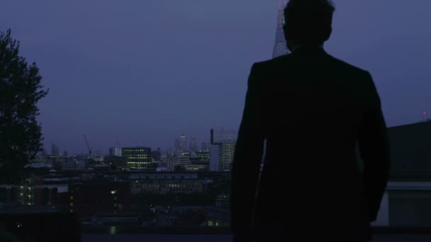 Başarılı bir iş adamı Londra şehir manzarası görünümü geceleri dışarı bakar — Stok video