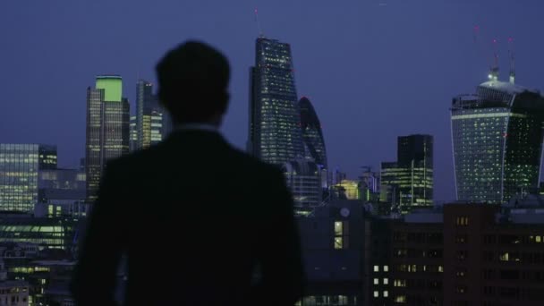 Erfolgreicher Geschäftsmann blickt bei Nacht auf die Skyline von London — Stockvideo