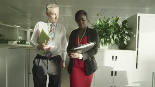 Empresario y mujer de negocios charlan juntos mientras caminan a través de la oficina moderna — Vídeos de Stock