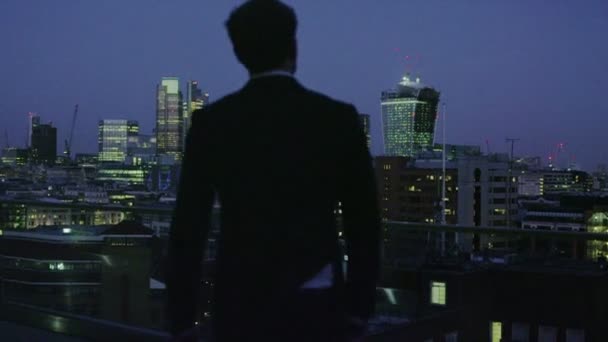 Erfolgreicher Geschäftsmann blickt bei Nacht auf die Skyline von London — Stockvideo