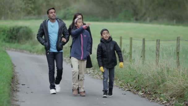 Glückliche vierköpfige Familie genießt einen Spaziergang durch eine lokale Grünfläche — Stockvideo