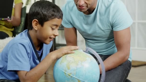 Vader en zoon met behulp van een wereldbol om te kijken naar landen over de hele wereld — Stockvideo