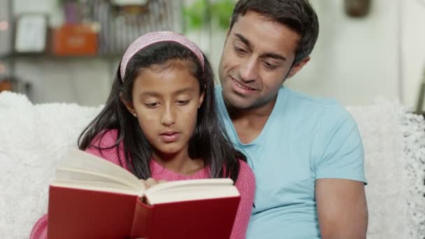 Um pai e sua filha passam um tempo juntos em casa, lendo um livro — Vídeo de Stock