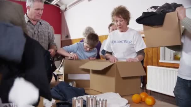 Charity volunteers and community members sort through donated food and clothing — Stock Video