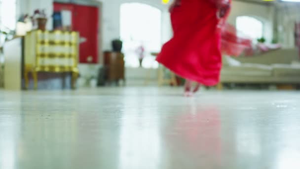 Mujer joven en un vestido rojo girando y bailando alrededor de su apartamento — Vídeo de stock