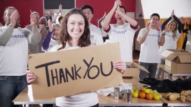 Trabalhadora da caridade sustenta um sinal de agradecimento enquanto seus colegas aplaudem — Vídeo de Stock