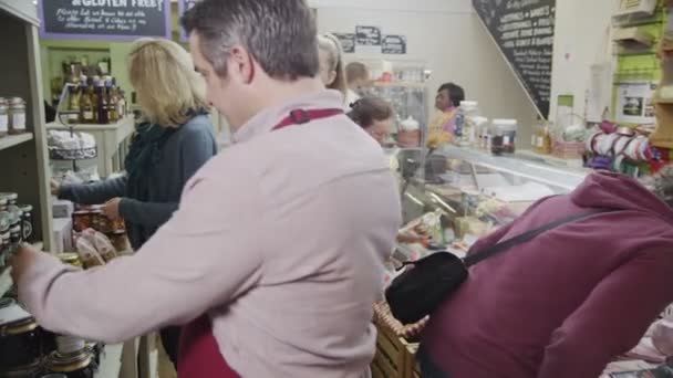 Employees working and shoppers browsing in a local delicatessen or food store. — Stock Video