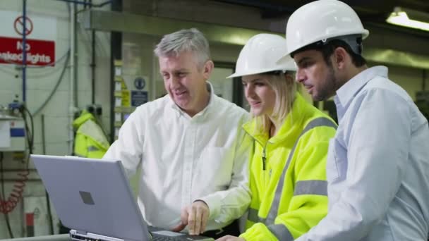 Drei Arbeiter in einem Lager mit Laptop diskutieren über ihre Arbeit. — Stockvideo