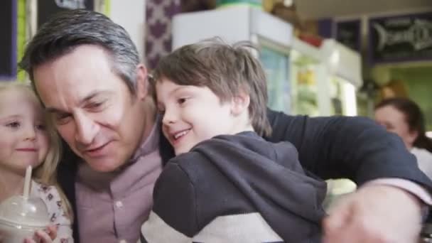 Söt ung pojke i ett café ger sin far en kram — Stockvideo